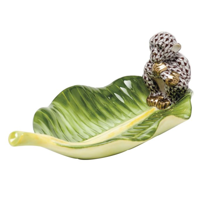 The Herend Monkey on Banana Leaf is a collectible porcelain dish, shaped like a green leaf with a decorative monkey on one end—an elegant piece for any setting.
