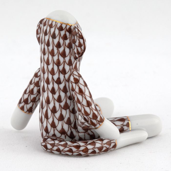 A Herend porcelain Sock Monkey figurine, hand painted with a brown and white scale-like pattern, is displayed on a white surface with its back facing the camera.