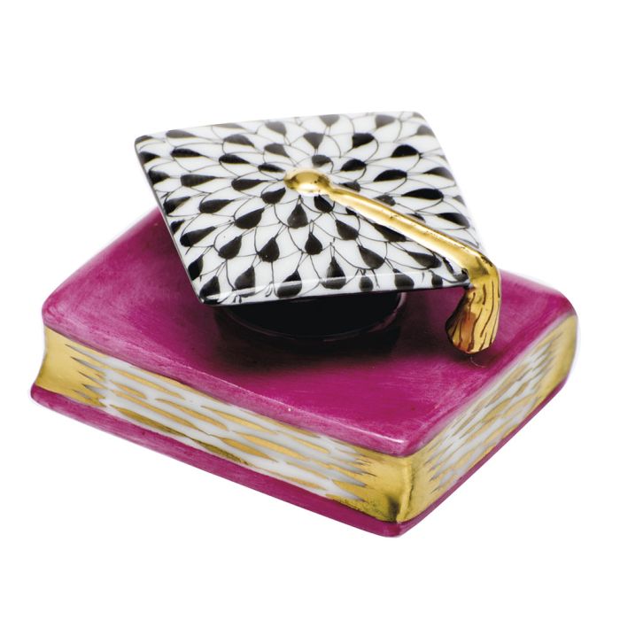 The Herend Graduation Cap is a decorative accent, featuring a pink and gold book topped with a black-and-white cap, adding timeless elegance and charm to any space.