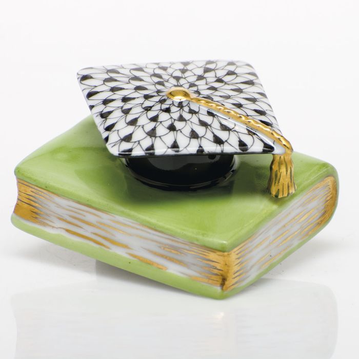 The Herend Graduation Cap is a collectible porcelain figurine featuring a green book with gold-edged pages and a black-and-white patterned cap with a gold tassel—a timeless decorative accent for any space.
