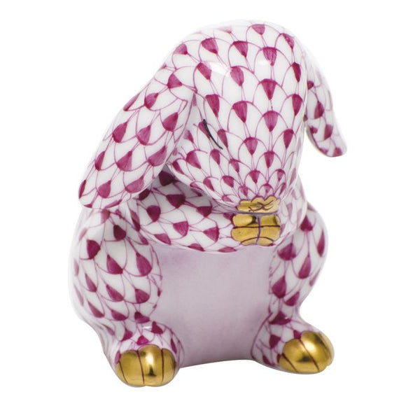 The Herend Praying Bunny figurine features a pink and white scale pattern, revealing its paws as it sits gracefully. Hand-painted with golden accents on its ears and feet, this exquisite piece enhances artistic appreciation.