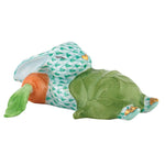 The Herend Slumber Bunny figurine, handcrafted in Hungary, depicts a patterned rabbit in the iconic fishnet motif, lying under a large green leaf with an orange carrot beside it.
