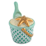 The Herend Beach Bucket is a hand-painted porcelain trinket box shaped like a sand bucket with a green patterned design, gold handle, starfish on the lid, and matching green shovel—a charming decorative accent.