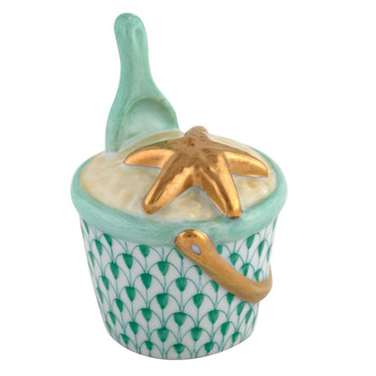 The Herend Beach Bucket is a hand-painted porcelain trinket box shaped like a sand bucket with a green patterned design, gold handle, starfish on the lid, and matching green shovel—a charming decorative accent.