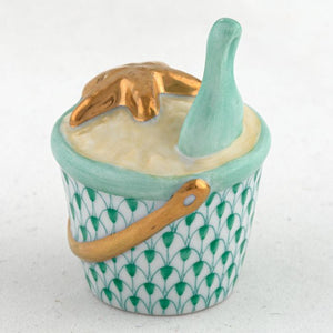 The Herend Beach Bucket is a hand-painted collectible porcelain figurine featuring a gold handle, gold starfish, green bottle, and green fish scale patterns—a charming decorative accent for any space.