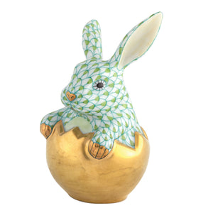 The Herend "Hatching Bunny" is a porcelain figurine of a green-patterned rabbit emerging from a gold egg shell, featuring hand-painted designs inspired by classic Herend porcelain.