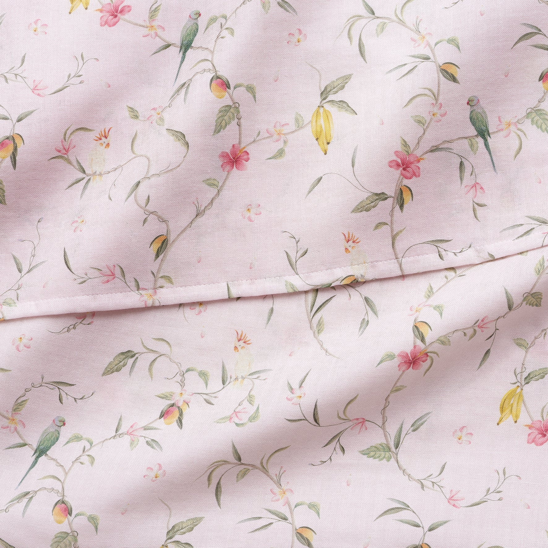 The Gooselings Dreaming of Paradise Swaddle features light pink 100% cotton with green birds, yellow and pink flowers, and green vines in a vintage style—slightly wrinkled and folded, ideal for a cozy baby blanket.