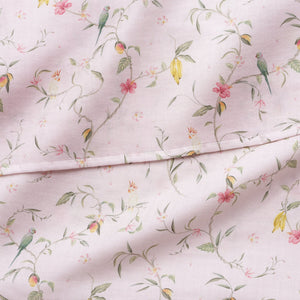 The Gooselings Dreaming of Paradise Swaddle features light pink 100% cotton with green birds, yellow and pink flowers, and green vines in a vintage style—slightly wrinkled and folded, ideal for a cozy baby blanket.