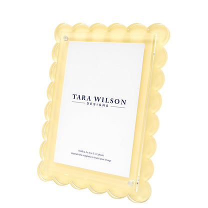 Brighten your decor with this yellow scalloped-edge photo frame from Tara Wilson Designs’ Scallop Frame Collection, featuring a clear front and a "Tara Wilson Designs" placeholder card. A cheerful best-seller for any space.