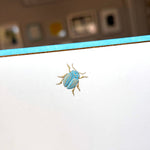 The Scarab Note Card Set by Printery features a blue and gold beetle illustration near the top edge of a pearl white card with a blue border.