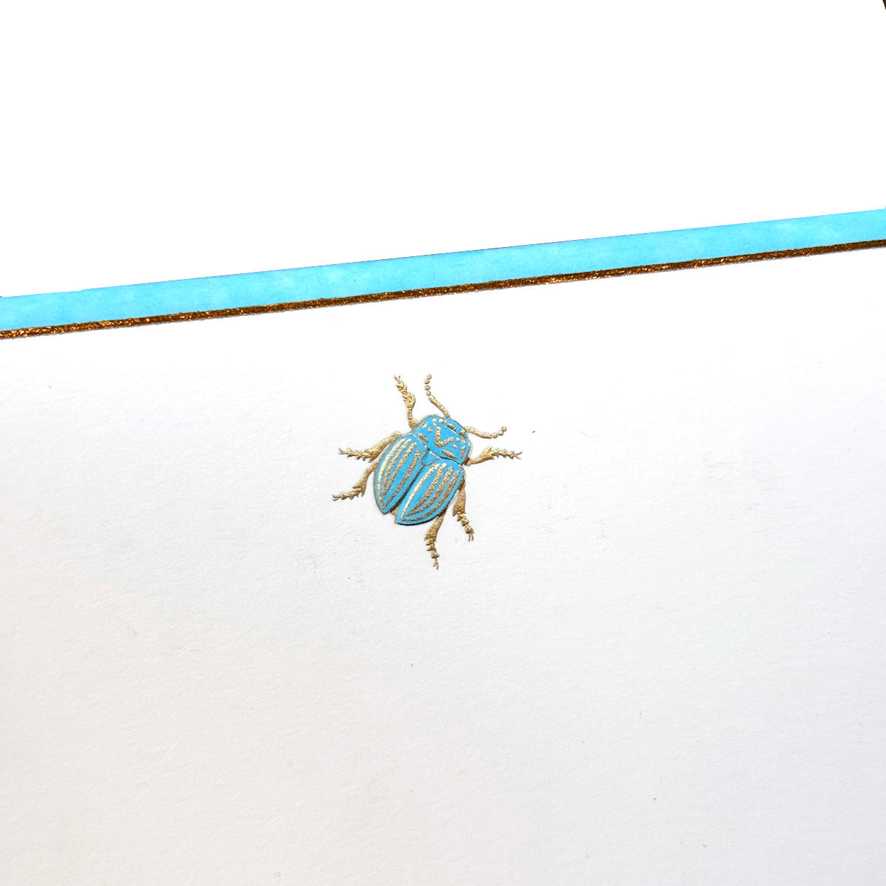Printery’s Scarab Note Card Set features a centered blue and gold beetle illustration on pearl white stationery, accented by a matching horizontal stripe.