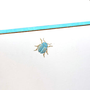 Printery’s Scarab Note Card Set features a centered blue and gold beetle illustration on pearl white stationery, accented by a matching horizontal stripe.