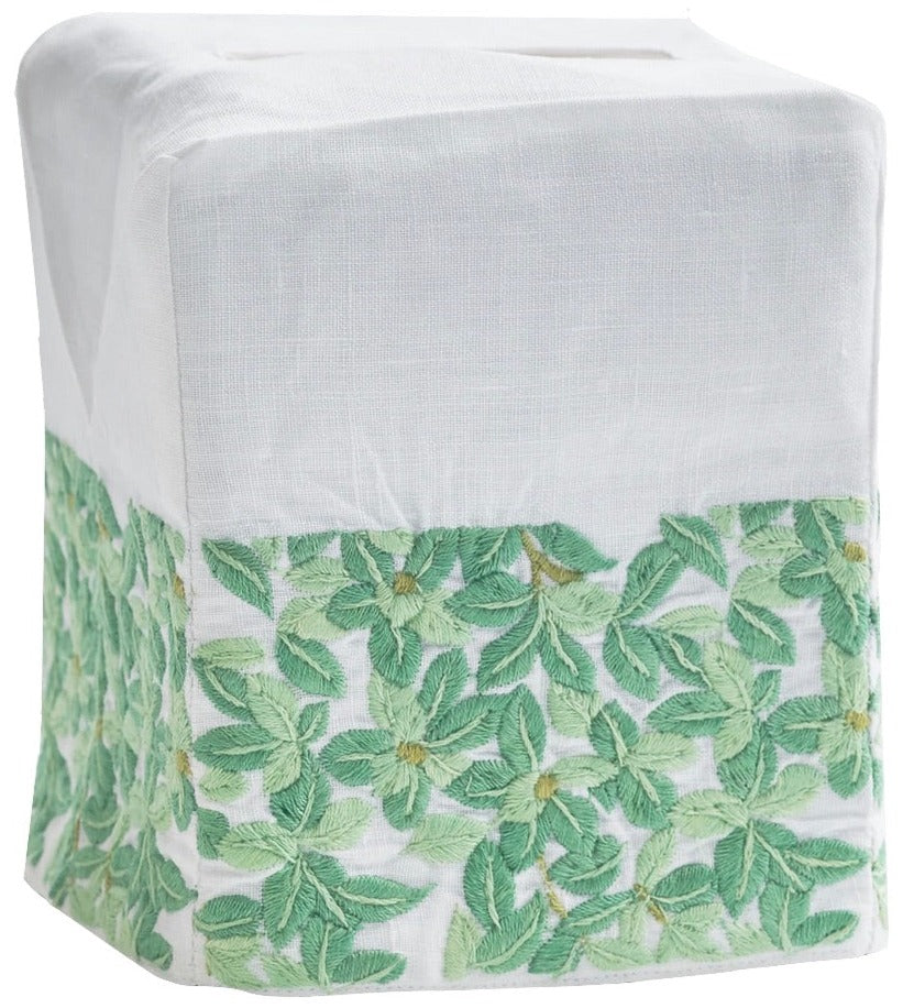 A white Italian linen tissue box cover from Haute Home’s Boxwood Bath Collection, featuring green leaf and flower embroidery along the bottom edge.