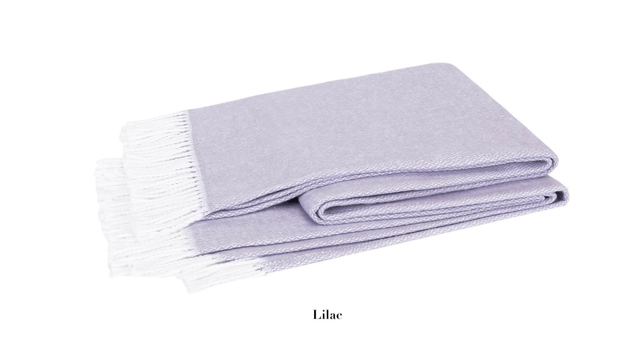The Matouk Pezzo Throw Collection by Matouk is a cozy, brushed cotton blanket in soothing lilac with elegant white fringes. It's OEKO-TEX Standard 100 certified for safety and sustainability against its crisp white backdrop.