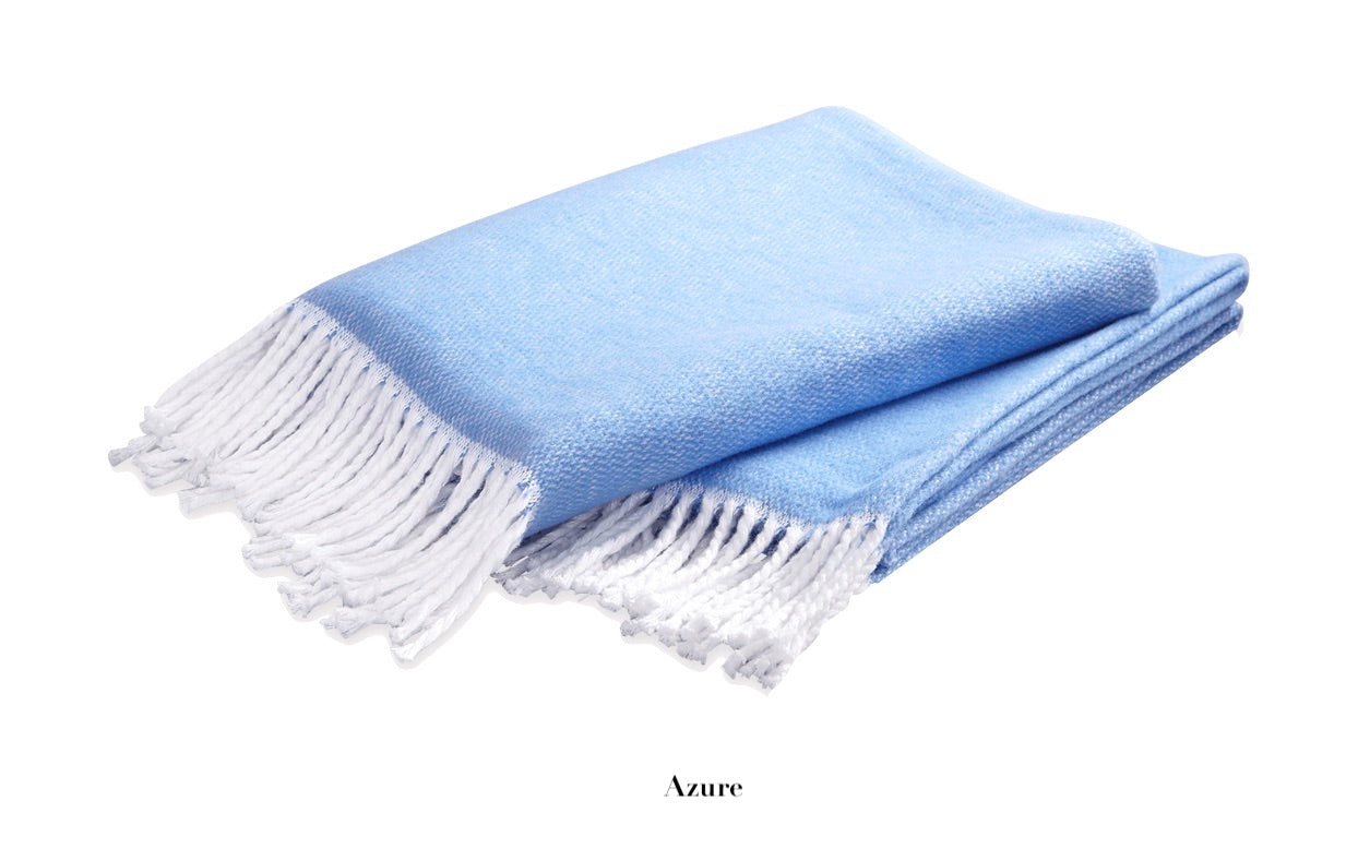 A neatly folded light blue Pezzo Throw by Matouk, crafted from brushed cotton with white fringed edges, displayed on a white background. "Azure" is written below the blanket.