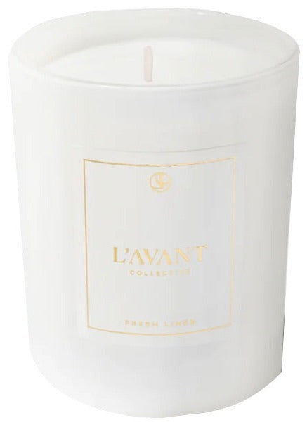 A white candle in a glass container with minimalist design, labeled L’Avant Collective, complements the Fresh Linen Scent Collection of luxurious hand soaps and laundry detergent.