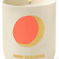 A lit scented candle with a minimalist design, featuring a red and gold circle motif and the words "Assouline Travel Candle Moon Paradise.