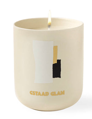 The Assouline Travel Candle Gstaad Glam, in a cream container with abstract white, gold, and black shapes and "Gstaad Glam" text, offers a winter escape vibe. Ideal for a Travel from Home Candle experience.