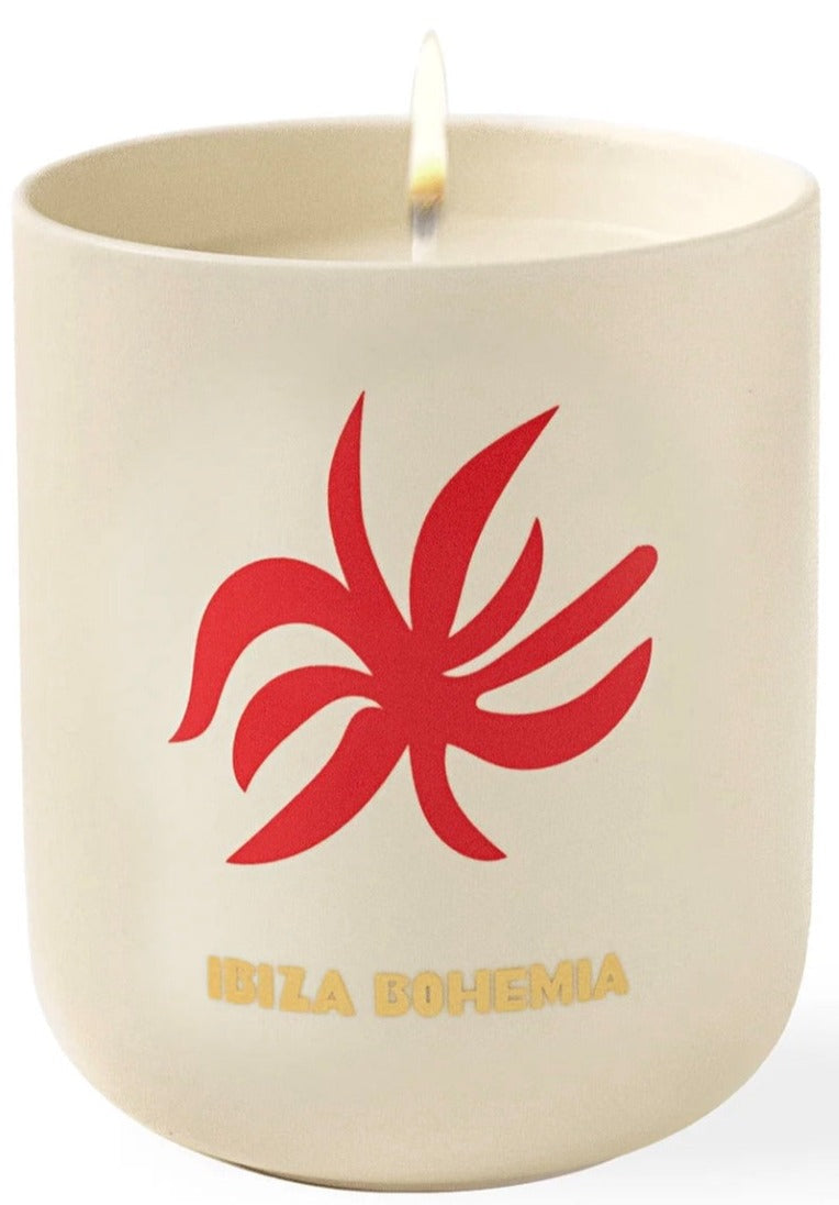 An Assouline Travel Candle Ibiza Bohemia sits in a beige container decorated with a red abstract design, releasing subtle patchouli undertones.