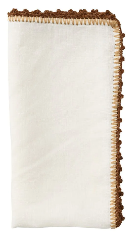 The Kim Seybert Knotted Edge Napkin Set features neatly folded white 100% linen napkins with brown decorative stitching, a hand-crocheted textured border, and elegant edging.