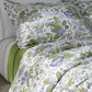 The Matouk Pomegranate Roman Linen Bedding Collection in Lilac features OEKO-TEX Standard 100 certified white sheets, pillowcases, and a comforter with a green, purple, and blue floral botanical pattern.