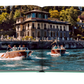 Two vintage wooden speedboats carrying passengers on a clear day on Lake Como Idyll, with a grand building on the waterfront in the background, by Assouline.