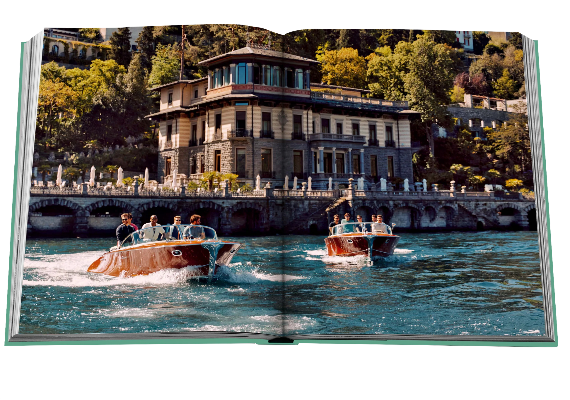 Two vintage wooden speedboats carrying passengers on a clear day on Lake Como Idyll, with a grand building on the waterfront in the background, by Assouline.