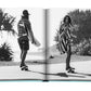 In the Assouline series titled *Byron Bay*, two individuals are captured riding skateboards along a palm tree-lined path. The person on the left carries a surfboard and is wearing a hat, while the other individual on the right has a longboard and holds a striped towel.
