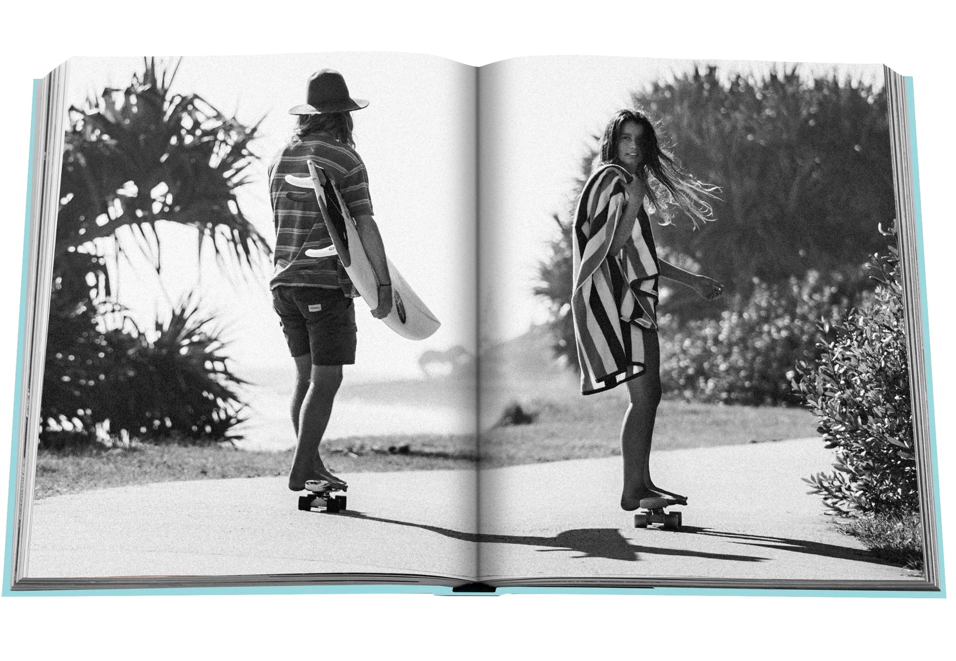In the Assouline series titled *Byron Bay*, two individuals are captured riding skateboards along a palm tree-lined path. The person on the left carries a surfboard and is wearing a hat, while the other individual on the right has a longboard and holds a striped towel.