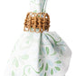 The Provence Napkin Ring by Juliska, crafted from hand-woven rattan, holds a white napkin with a light green floral pattern, bringing natural charm to your table setting.