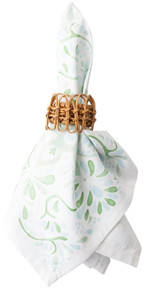 The Provence Napkin Ring by Juliska, crafted from hand-woven rattan, holds a white napkin with a light green floral pattern, bringing natural charm to your table setting.