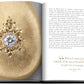An open book titled "Jewelry Guide: The Ultimate Compendium" by Assouline displays an ornate piece of jewelry with a large gemstone on the left page, crafted from gleaming precious metals, and text on the right page, ending with a quote attributed to Andrea Bucellari, a jeweler.