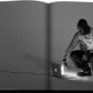 A man leans down to touch a laptop illuminated in the dark on the pages of an open book, while beside him rests an exquisite piece from the Louis Vuitton Virgil Abloh Ultimate Edition by Assouline.