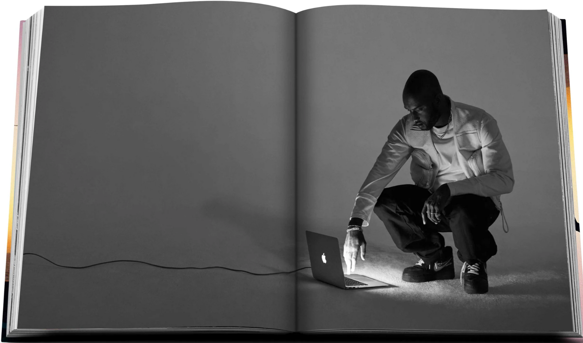 A man leans down to touch a laptop illuminated in the dark on the pages of an open book, while beside him rests an exquisite piece from the Louis Vuitton Virgil Abloh Ultimate Edition by Assouline.