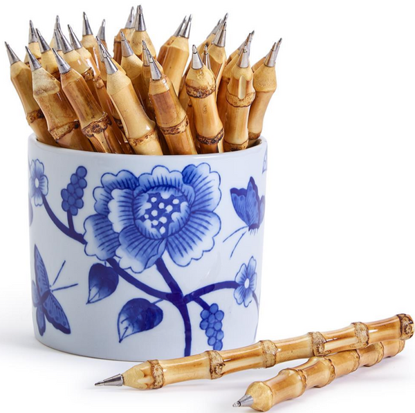 A collection of Two's Company bamboo pens in a blue and white porcelain vase with one pen lying in front of it.