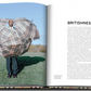 Open magazine showcases a man inside a large, plaid umbrella on a grassy field, highlighting British style and the luxury brand's influence. The right page features the text "Britishness," embodying elegance and tradition. This imagery complements the Burberry Book by Assouline.