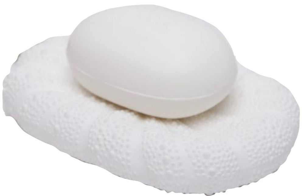 A white soap sits on the Hilo Bath Collection’s textured oval porcelain dish by Pigeon & Poodle, both in shades of white with a subtle sea urchin motif, against a plain background.