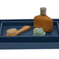 A blue tray from Pigeon & Poodle's Dannes Bath Collection in faux waxed Belgian linen holds a wooden brush, green soap bar, and a wicker-wrapped bottle—an elegant bath triple threat.