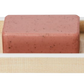 A pink soap bar with dark specks rests in a light painted wood soap dish from the Maranello Bath Collection by Pigeon & Poodle.