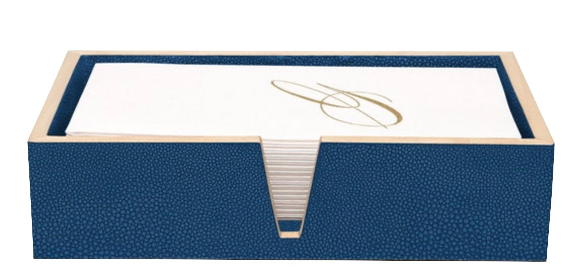The Manchester Bath Collection by Pigeon & Poodle features a blue shagreen-textured napkin holder with white napkins accented by a gold cursive letter design.
