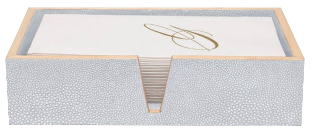 A stack of white napkins with a gold "S" monogram rests in a textured light gray rectangular holder from the Manchester Bath Collection by Pigeon & Poodle, featuring elegant shagreen veneer trim.
