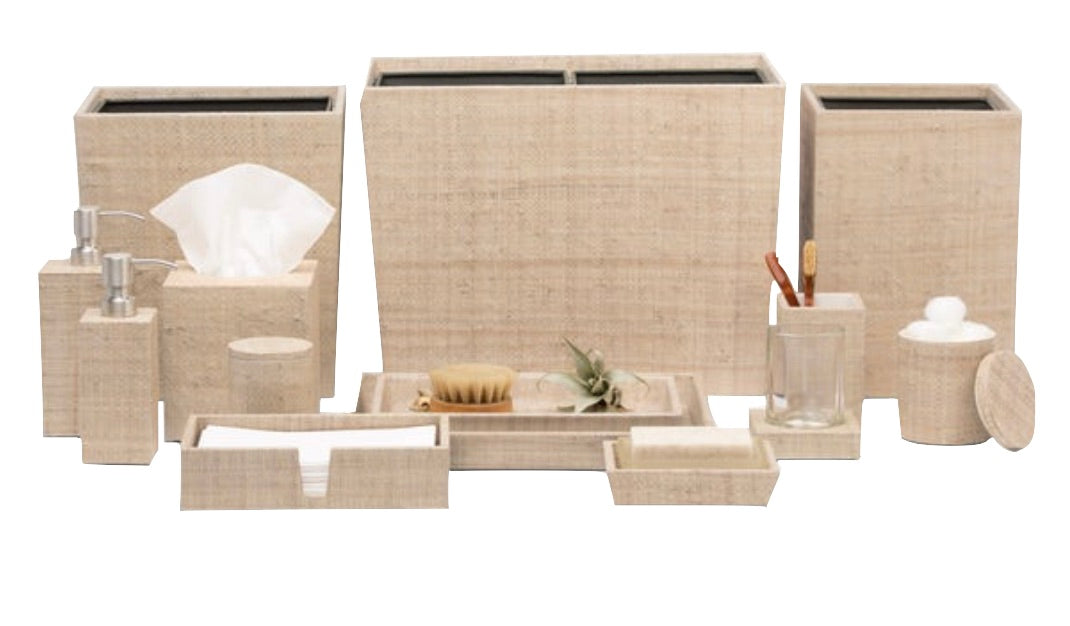 The Ghent Bath Collection by Pigeon & Poodle features beige woven grass accessories—tissue box, wastebasket, trays, containers, soap dispenser, and jars—arranged for a relaxed seaside-chic look on a white background.