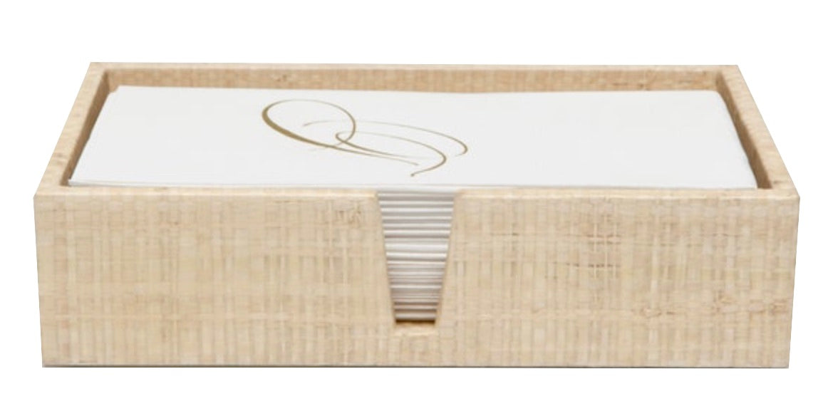 A rectangular woven grass box by Pigeon & Poodle holds white napkins with a gold design—an elegant accent from the Ghent Bath Collection, perfect for bringing seaside-chic style to your bathroom.