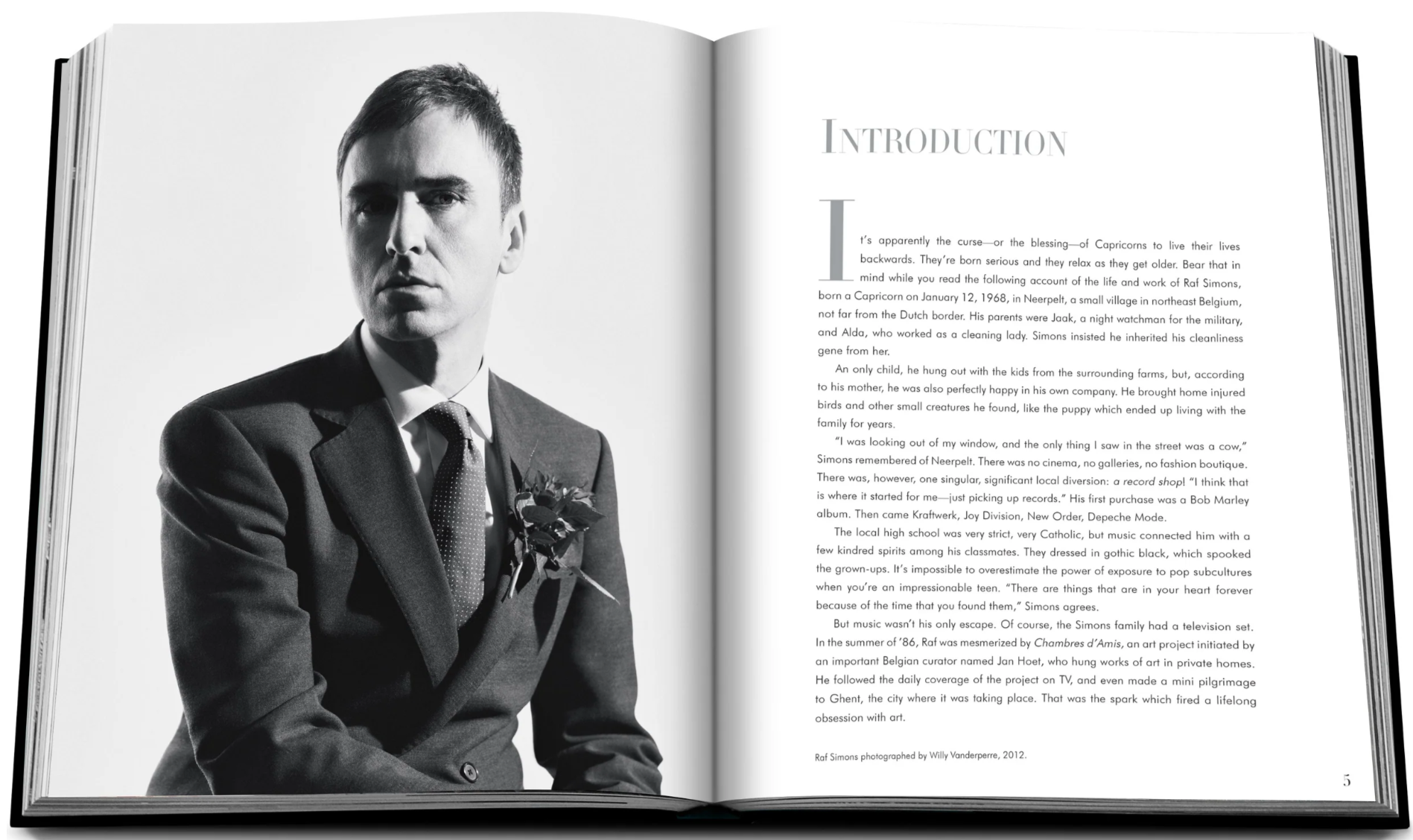 A black and white image shows an open book with a photo of a man in a suit on the left page and text beginning with "Introduction" on the right. Perfect for fashion enthusiasts, this piece introduces the world of haute couture, reminiscent of Assouline's Dior by Raf Simons 2012 - 2015 elegant designs.