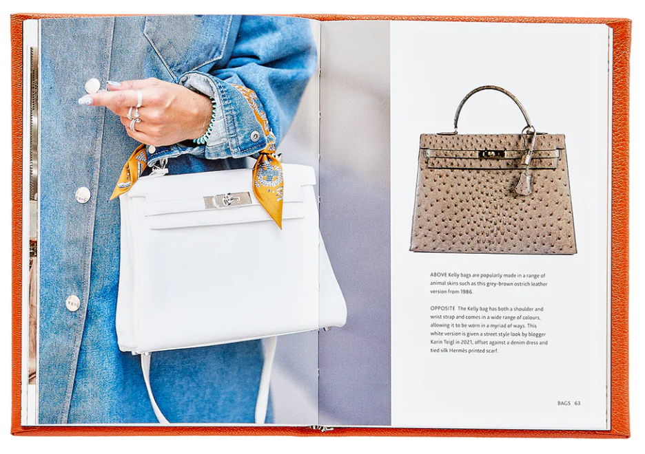 A person in a denim jacket holds a white handbag adorned with a scarf, embodying the essence of luxurious accessories. An open book titled "Little Book of Hermes" by Graphic Image reveals a photo of a brown Hermès handbag on one page, capturing the keen eye of any fashion historian.