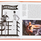 The open book reveals a vintage Hermès advertisement on the left and a text passage accompanied by an image of a horse sculpture on the right. Ideal for any fashion historian, the Little Book of Hermès by Graphic Image, with its distinctive orange cover, stands out against the white background, embodying the essence of timeless luxury accessories.