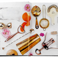 An open book, displaying the "Celebrate Rose" from Graphic Image, elegantly showcases gold and silver bar tools alongside pink flowers and rosé cocktails on a white background, offering ideal party inspiration.