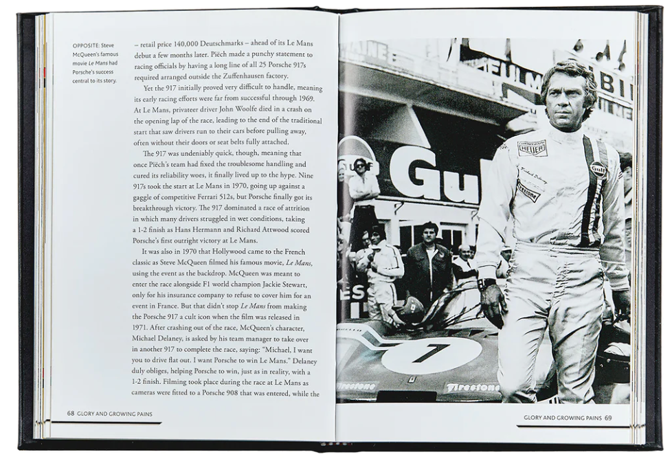 The open book, "The Story Of Porsche Black Leather" by Graphic Image, shows text about Steve McQueen's racing and the film "Le Mans" on the left page. On the right, there’s a black-and-white photo of a driver in racing gear beside a luxury Porsche race car.
