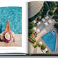 An open book from Assouline's "Hotel Wailea" displays a serene scene of a person sporting a hat and pink flowers sitting by a pool on the left page, while the right page features an aerial view of a lush pool area surrounded by greenery and loungers, perfectly embodying the tranquil atmosphere of this Maui boutique resort.