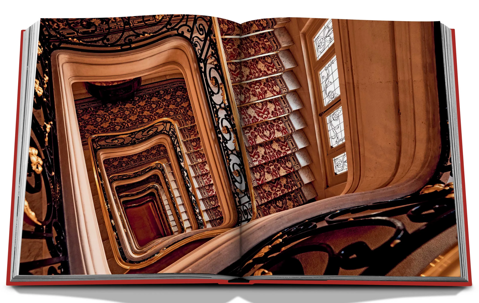 Open book displaying a photograph of the ornate spiral staircase at Plaza Athenee, with intricate railing and patterned wallpaper, taken from the top looking downwards through multiple levels—a testament to French hospitality by Assouline.